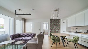 Una sala moderna con un sofá, dos sillones, una mesa redonda y una zona de cocina con armarios y una encimera.
