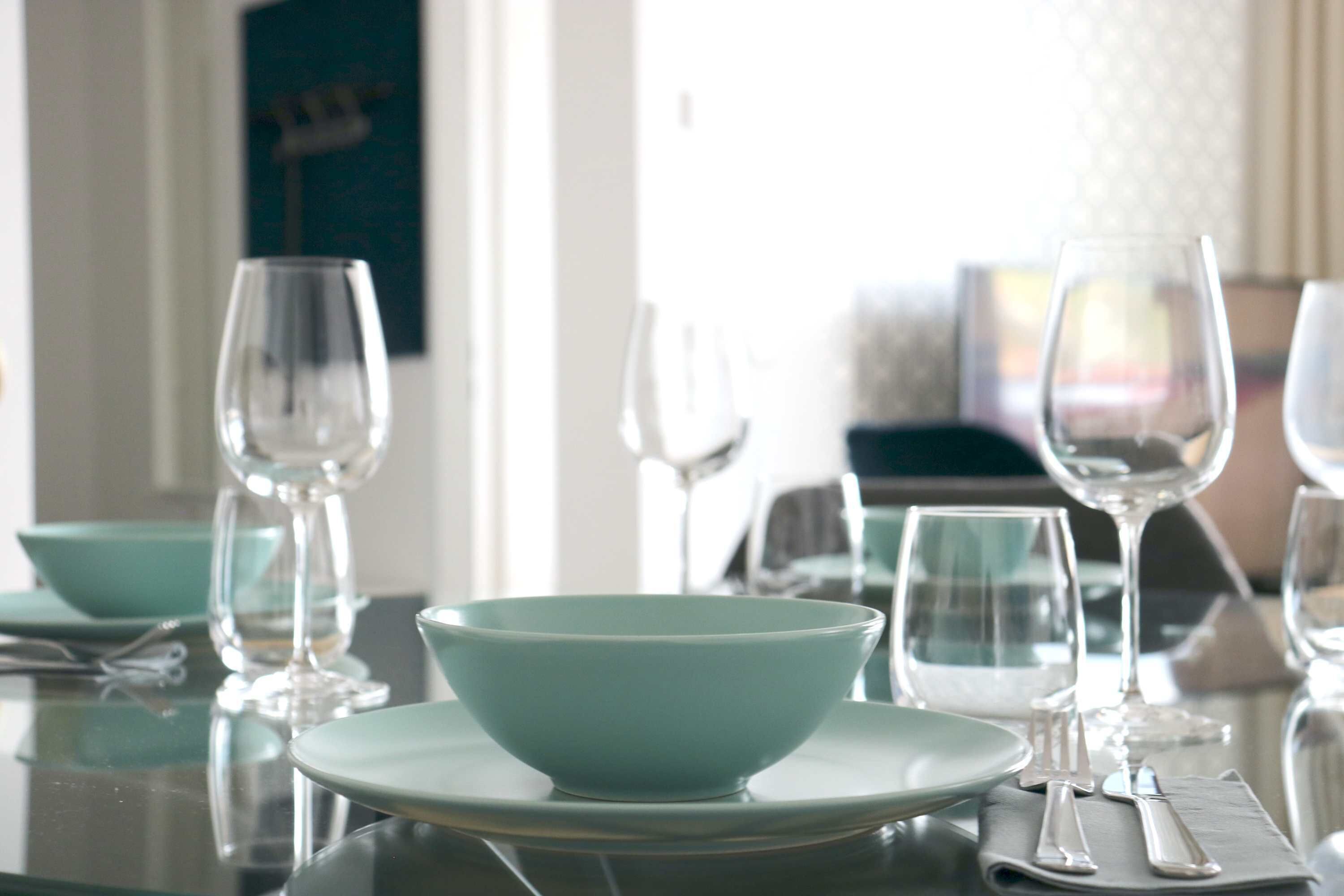 A dining table set with clear glassware and teal-colored bowls and plates.