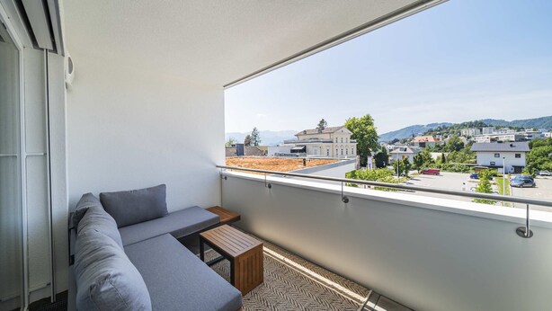 Un balcon avec un canapé, une petite table et une vue sur la ville et les collines.
