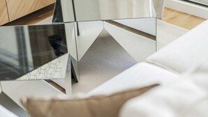 Un salon moderne avec une table basse en verre, un canapé agrémenté d’un plaid à motifs et un téléviseur posé sur un meuble en bois.