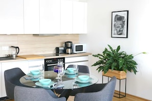 A modern kitchen with white cabinets, a microwave, a coffee maker, and a dining table set with blue bowls and wine glasses. - 3 Zimmer Apartment mit Blick auf die Stadt (Gmunden)