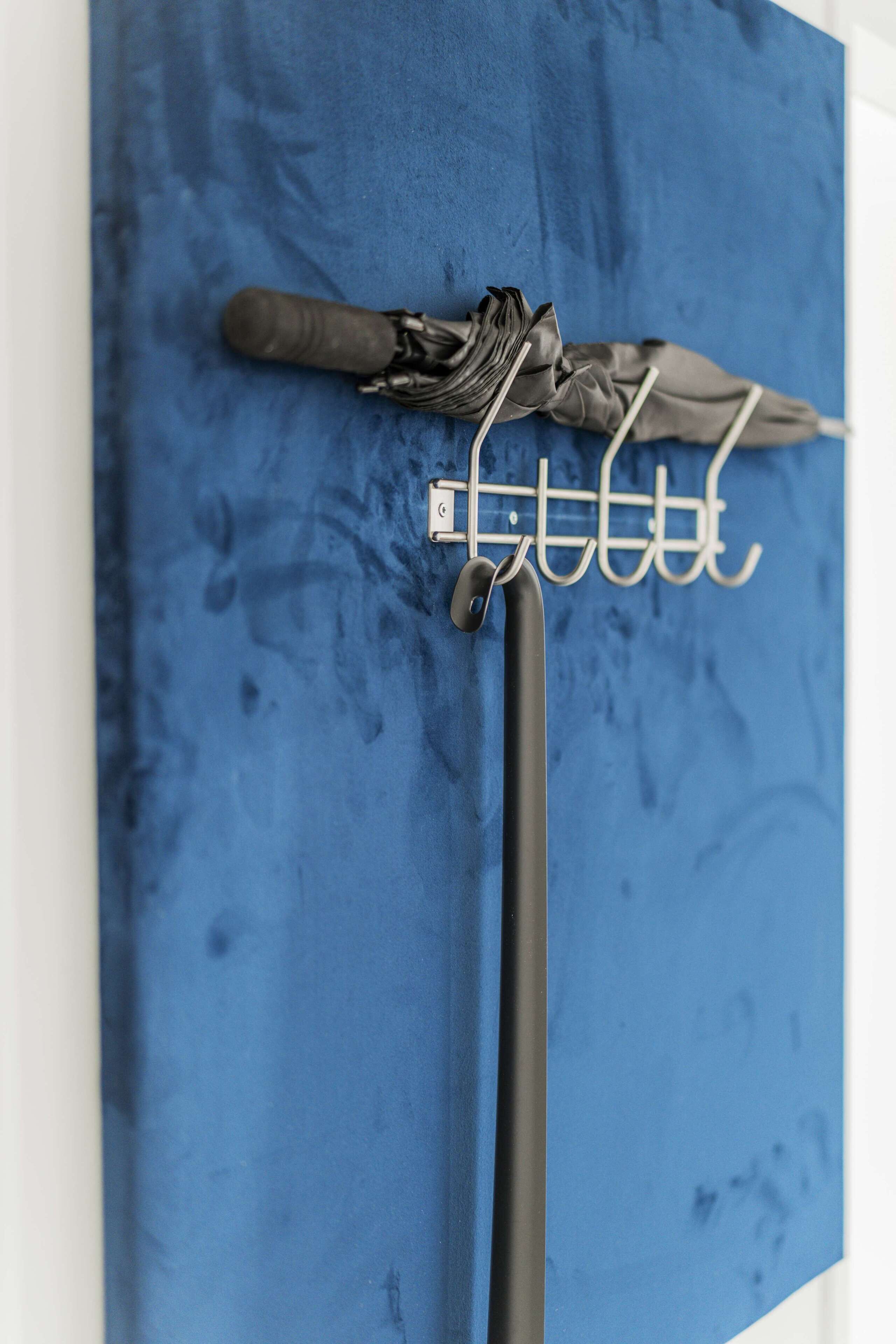 Eine blaue Wand mit einem Metallregal, das einen schwarzen Regenschirm und ein schwarzes Objekt trägt.