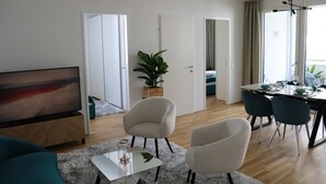 Een moderne woonkamer met een flatscreen televisie, een bank, een salontafel en een eethoek met stoelen en een tafel.
