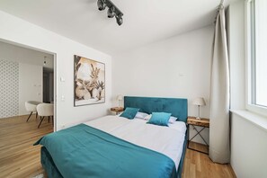 Un dormitori modern amb un llit, una taula de treball, una cadira i un quadre a la paret.