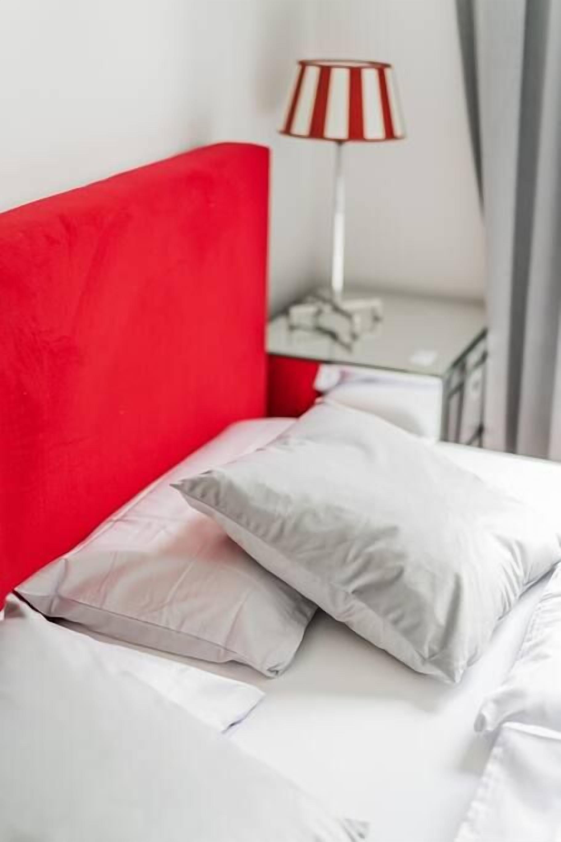 A bed with a red headboard, white bedding, and a striped lamp on a bedside table.