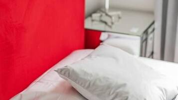 A bed with a red headboard, white bedding, and a striped lamp on a bedside table.