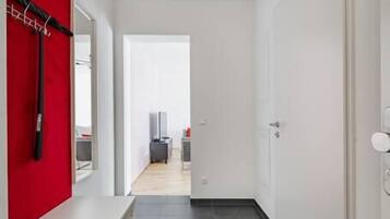 Un pasillo moderno con una pared de acento roja, una puerta blanca y vistas a una habitación con cama y televisión.