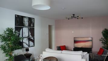 A modern living room with a glass coffee table, a white sofa with red cushions, a flat-screen TV, and a large abstract painting on the wall.