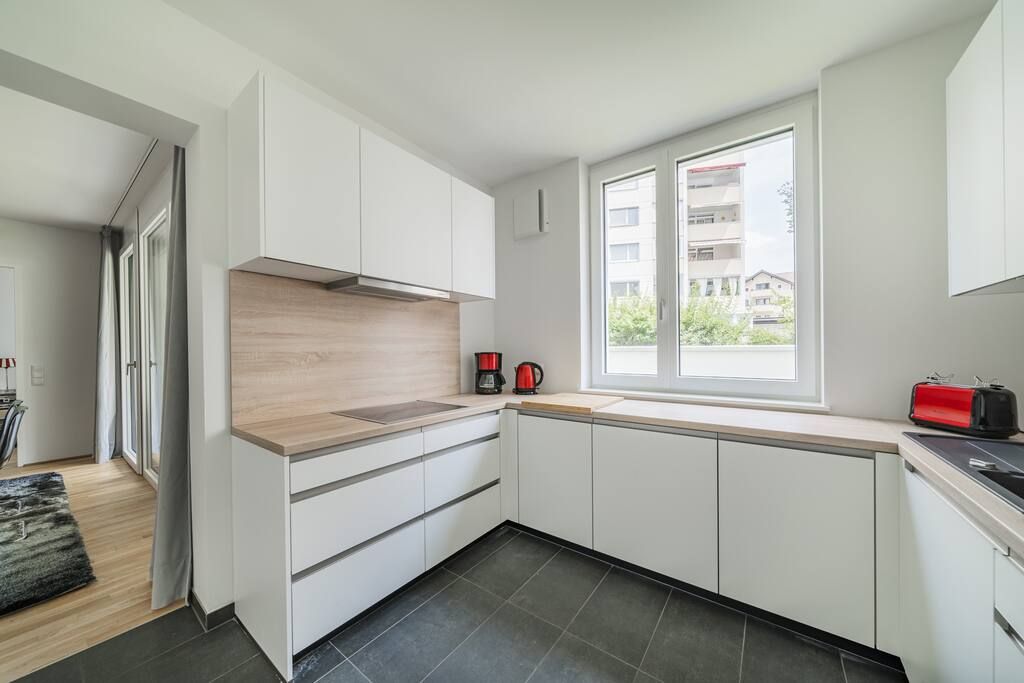 A modern kitchen with white cabinets, a wooden countertop, and a window with a view of buildings.
