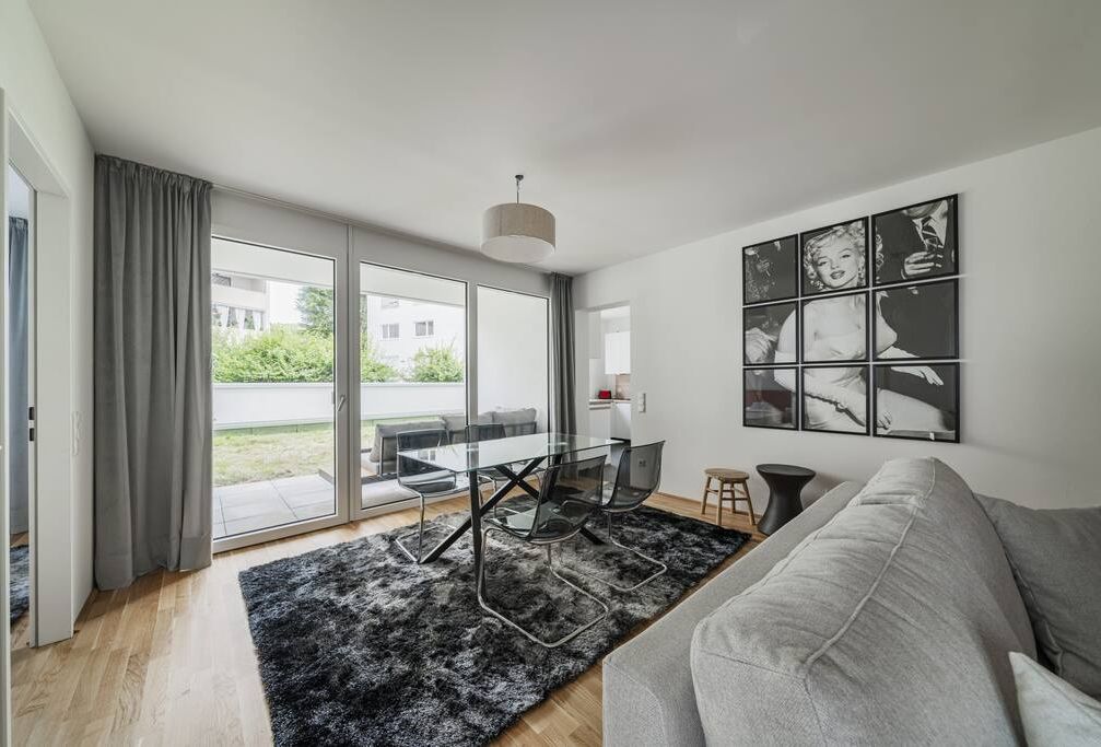 Una sala de estar moderna con una mesa de comedor de cristal, un sofá gris y una alfombra negra.