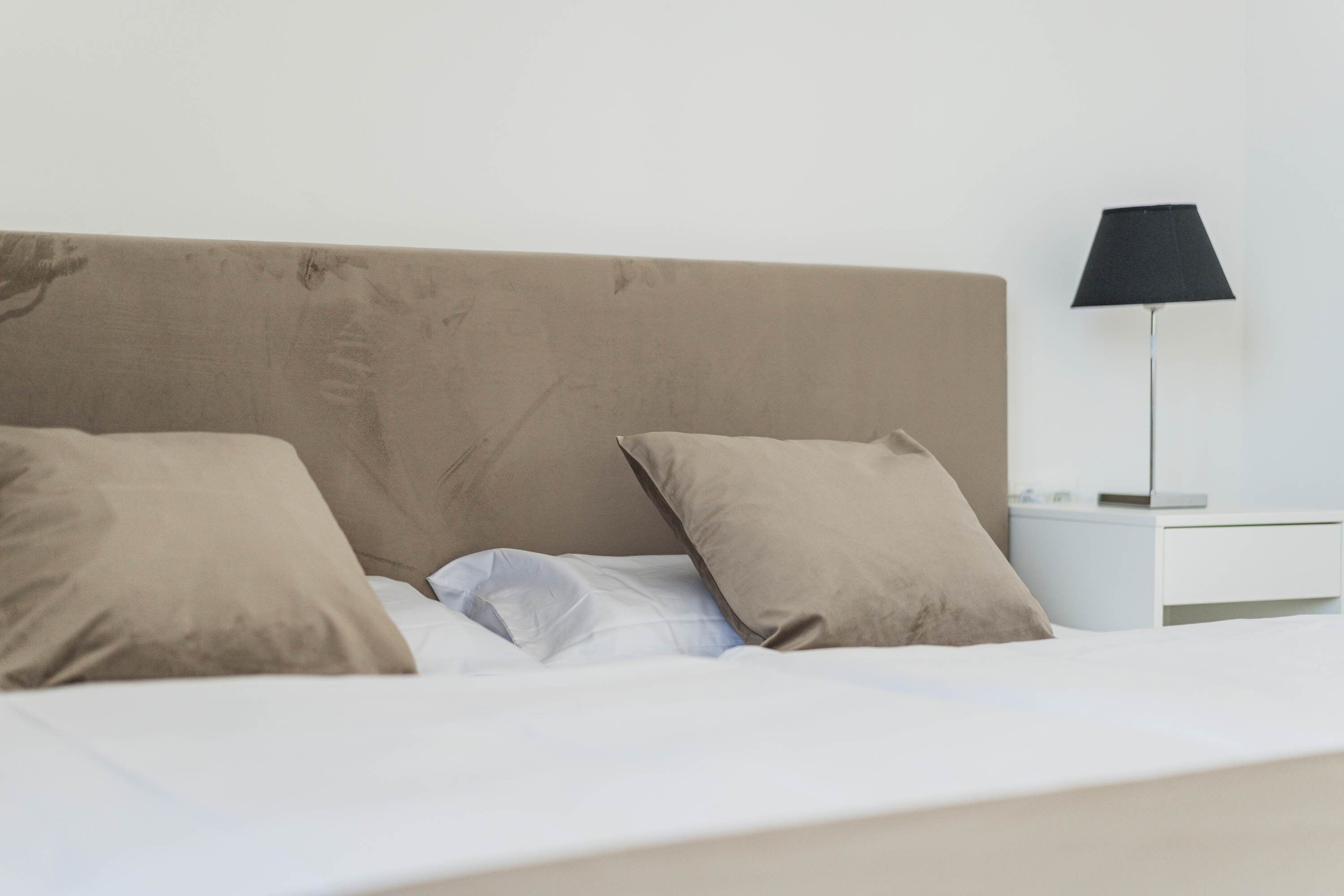 A bed with a headboard, two pillows, a white bedside table, and a lamp.