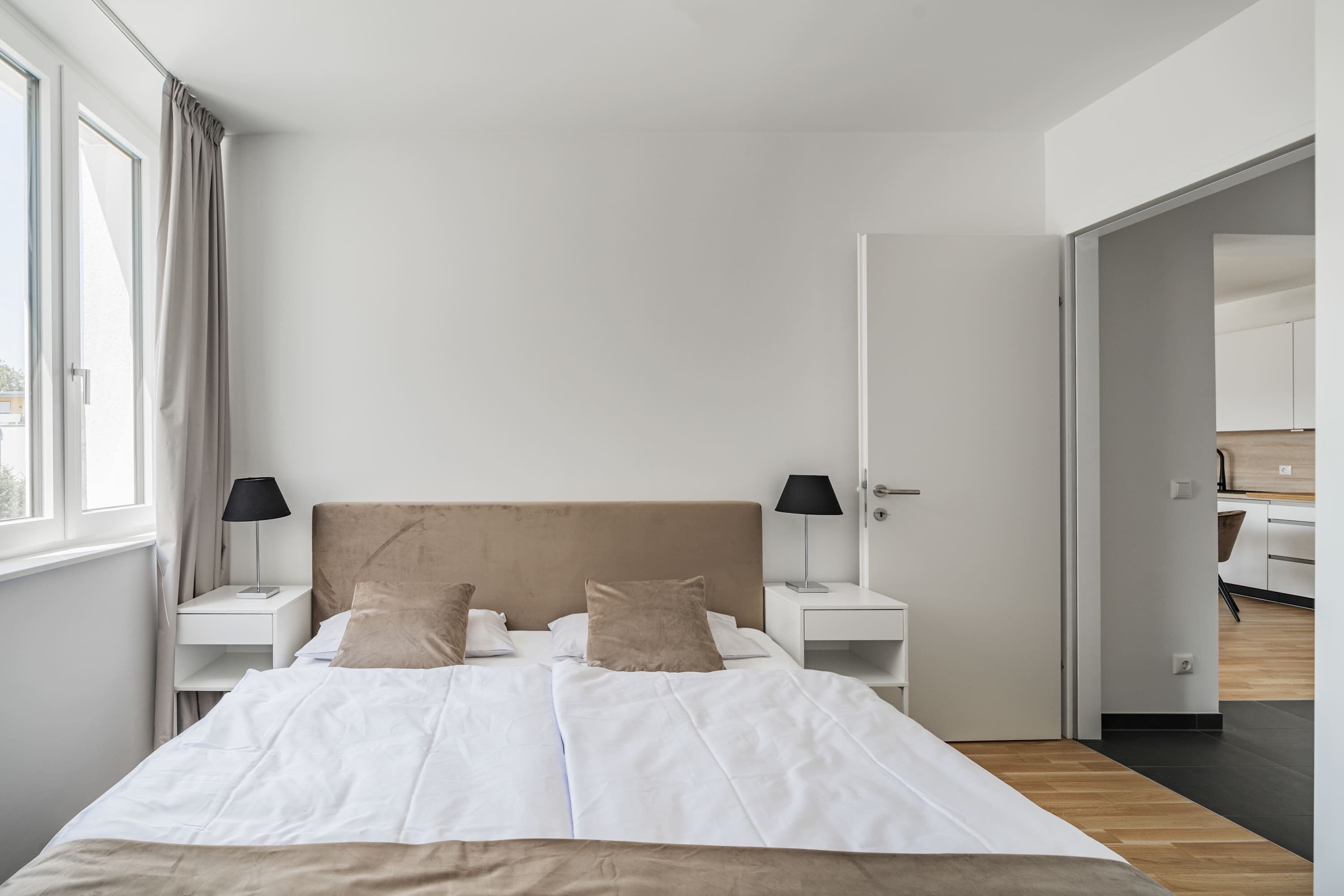 Camera moderna con un letto grande, due comodini con lampade, un armadio e vista su una cucina.