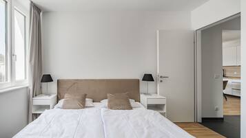 Camera moderna con un letto grande, due comodini con lampade, un armadio e vista su una cucina.