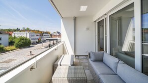 A balcony with a sofa, a small table, and a view of the street and buildings. - 3 Zimmer Apartment mit Blick auf die Stadt (Gmunden)