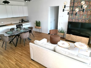 Una sala de estar moderna con un sofá, una mesa de comedor con sillas, un televisor y una cocina con armarios y electrodomésticos.