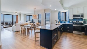 Une cuisine moderne dotée d’un grand îlot central, d’appareils électroménagers intégrés et offrant une vue sur l’extérieur.
