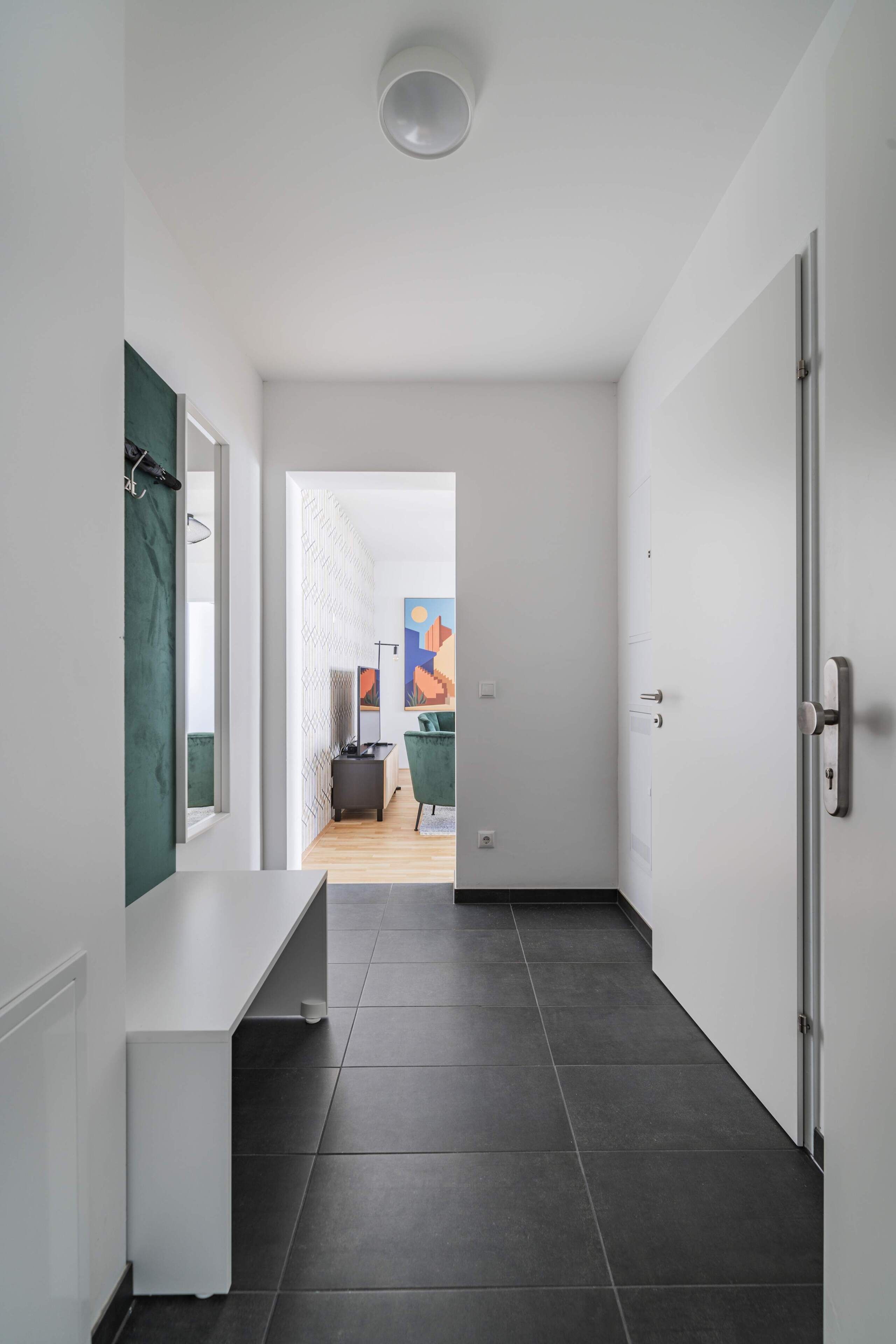 Un pasillo moderno con un banco blanco, una puerta y vistas a una habitación con cama y un cuadro.