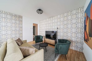 Una sala de estar moderna con un sofá, dos sillones, una mesa de centro y un televisor.
