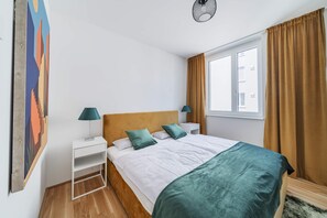 Un dormitorio con una cama, dos mesitas de noche, una ventana con cortinas y una obra de arte colgada en la pared.