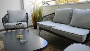 A modern outdoor seating area with a sofa and chairs, a table with a glass, and a potted plant.