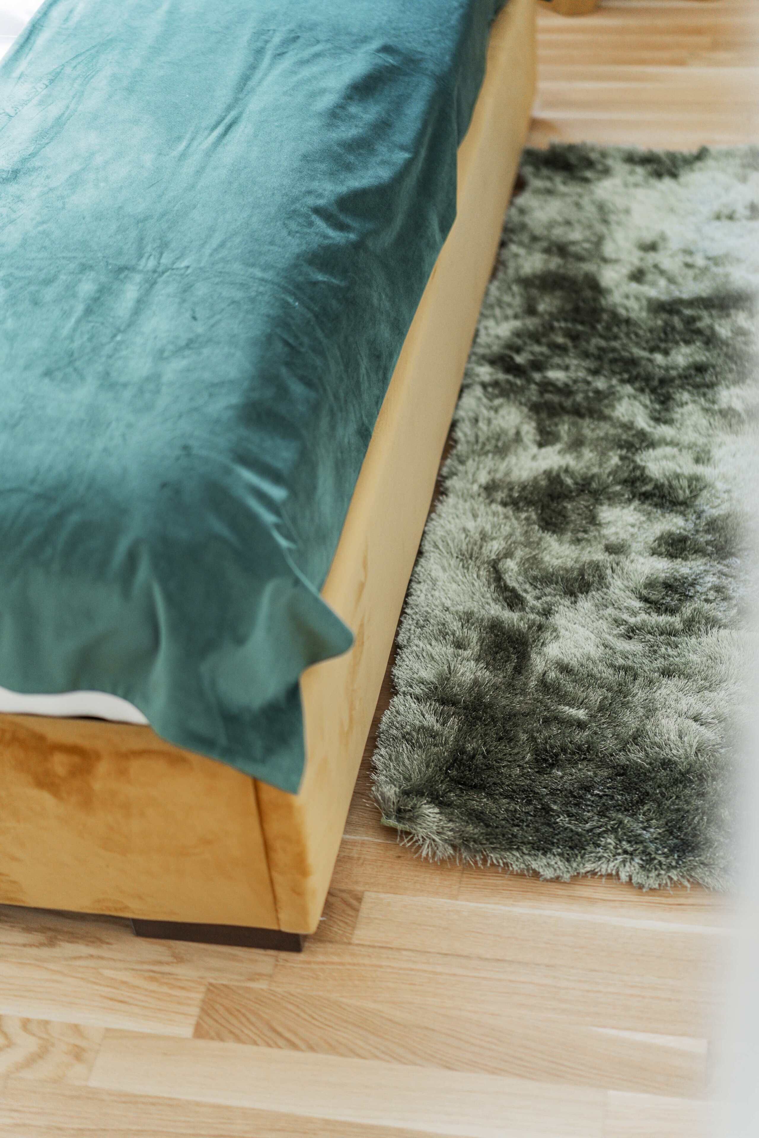 Una cama con un cojín azul turquesa y una alfombra de pelo gris sobre un suelo de madera.