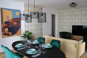 A dining area with a black table, teal chairs, and a sofa with green and beige cushions.