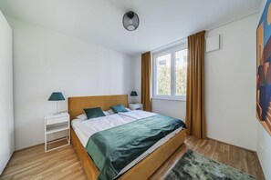 A bedroom with a bed, nightstands, a window with curtains, and a painting on the wall.