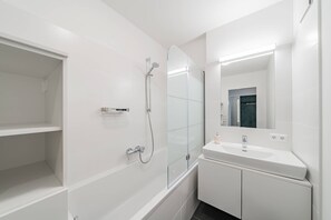 Un baño moderno con cabina de ducha de vidrio, lavamanos blanco y espejo.