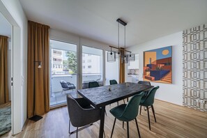 A modern dining area with a wooden table, green chairs, and a large window with curtains.