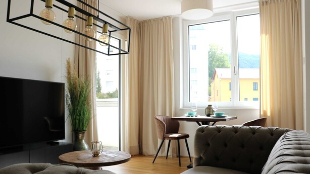 Moderni olohuone, jossa on sohva, televisio, ruokapöytä tuoleineen, ruukkukasvi ja ikkuna, jossa on verhot.