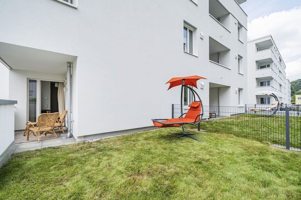 Un bâtiment moderne doté d’un toit plat, d’un espace extérieur abrité avec des chaises, et d’un jardin clôturé.
