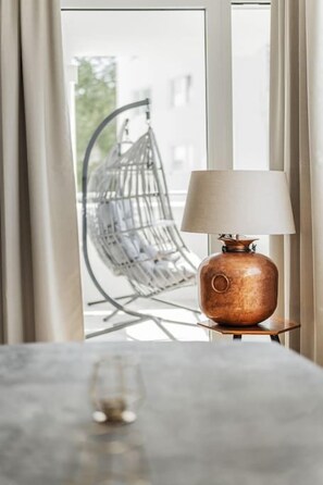 A table with a lamp and a glass, near a window with a view of a hanging chair and a building outside. - Two-room apartment with balcony and lake view – Trau(M)seeblick (Gmunden)