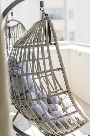 A hanging chair with a woven frame and cushions, suspended from a ceiling. - Two-room apartment with balcony and lake view – Trau(M)seeblick (Gmunden)