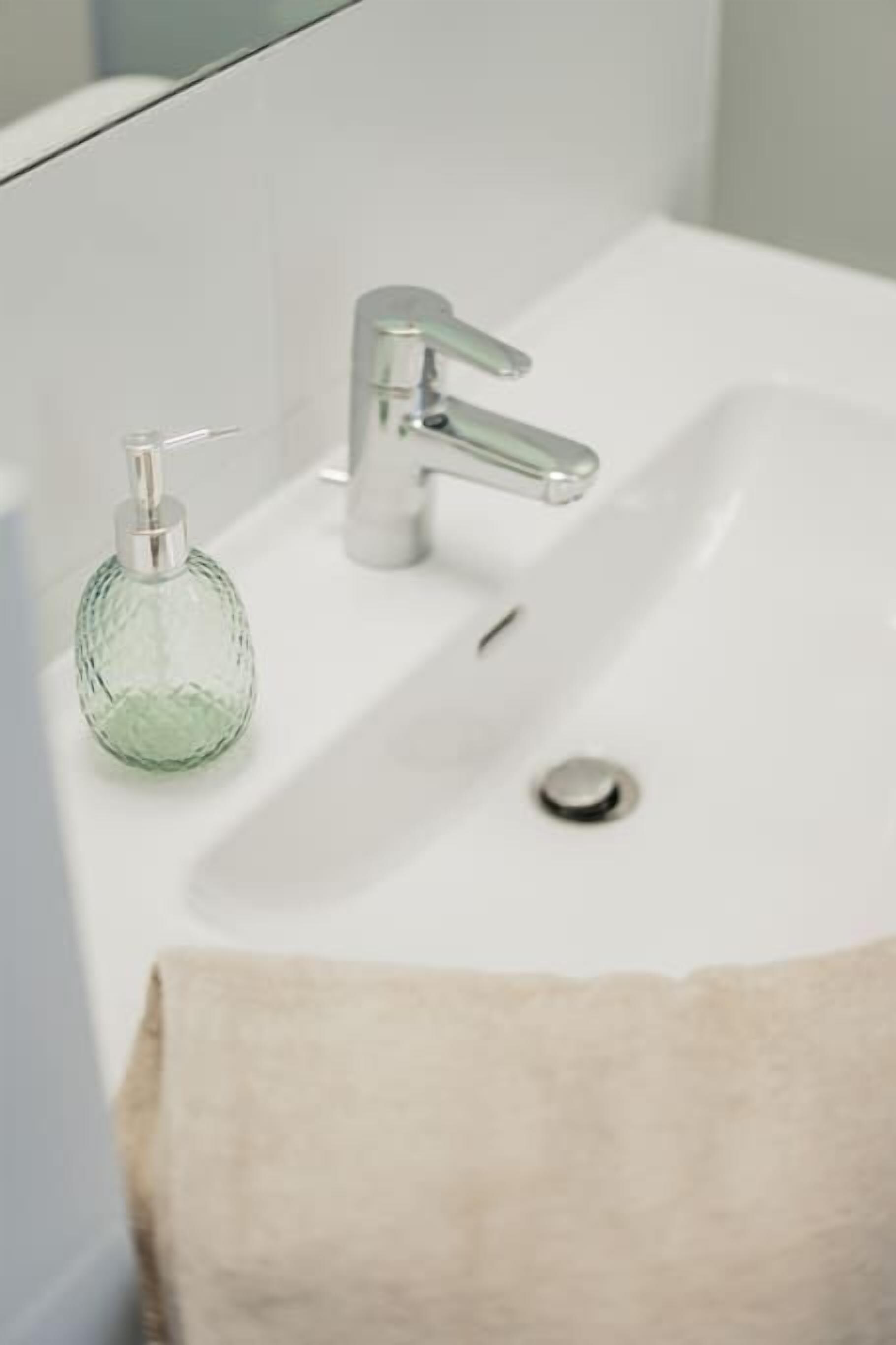 Un lavabo de salle de bain avec un distributeur de savon en verre et une serviette beige.
