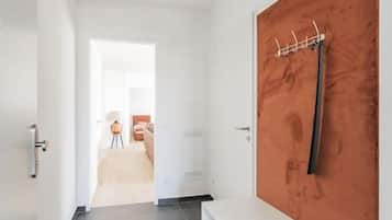 Ein Flur mit einer weißen Bank, einer Holztür mit Kleiderhaken und Blick in einen weiteren Raum.