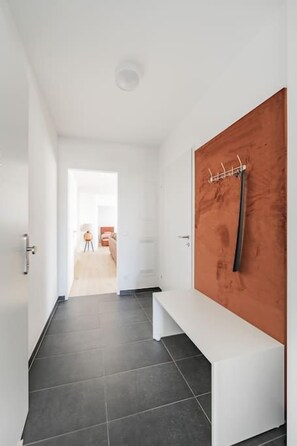 A hallway with a white bench, a wooden door with a coat rack, and a view into another room. - Two-room apartment with balcony and lake view – Trau(M)seeblick (Gmunden)