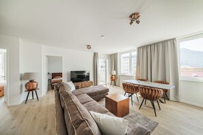 A modern living room with a sofa, TV, dining table, and chairs. - Two-room apartment with balcony and lake view – Trau(M)seeblick (Gmunden)