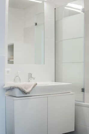 A modern bathroom with a glass shower enclosure, a white sink with a mirror above it, and a towel on the sink. - Two-room apartment with balcony and lake view – Trau(M)seeblick (Gmunden)