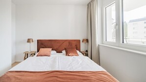 Et hotelværelse med en stor seng, to sengeborde med lamper og et vindue med gardiner.