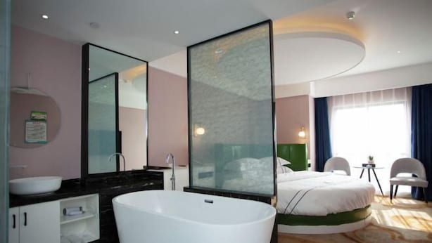 A modern hotel room with a large bathtub, a separate vanity, a large bed, and a small table with chairs. - Changxing Hainabaichuan Hotel (Changxing)