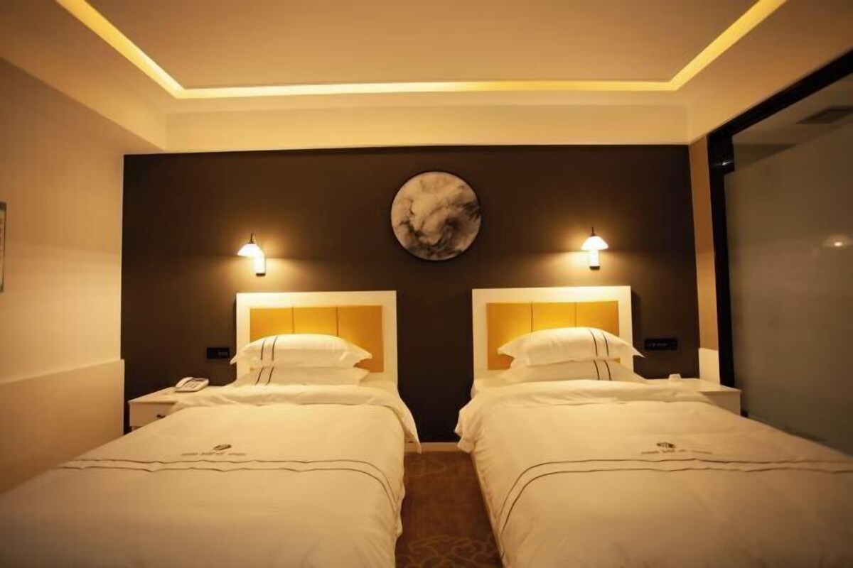 Ett hotellrum med två sängar, ett runt konstverk på väggen och två sänglampor.