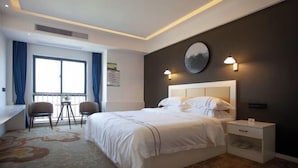 A hotel room with a bed, bedside tables, a desk, two chairs, a large window with curtains, and wall-mounted lighting. - Changxing Hainabaichuan Hotel (Changxing)