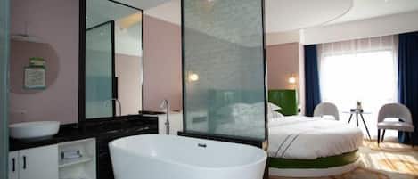 Una habitación de hotel moderna con una bañera grande, un tocador independiente, una cama amplia y una pequeña mesa con sillas.