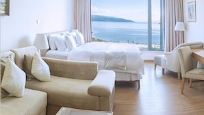 A hotel room with a bed, a sofa, a chair, a coffee table, and a large window with a view of the sea. - Huzhiyun Hotel (Chengjiang)
