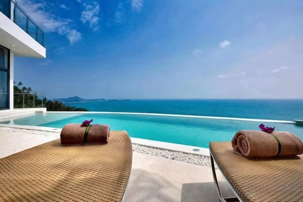 Zona de piscina con sillas de descanso y vista al mar.