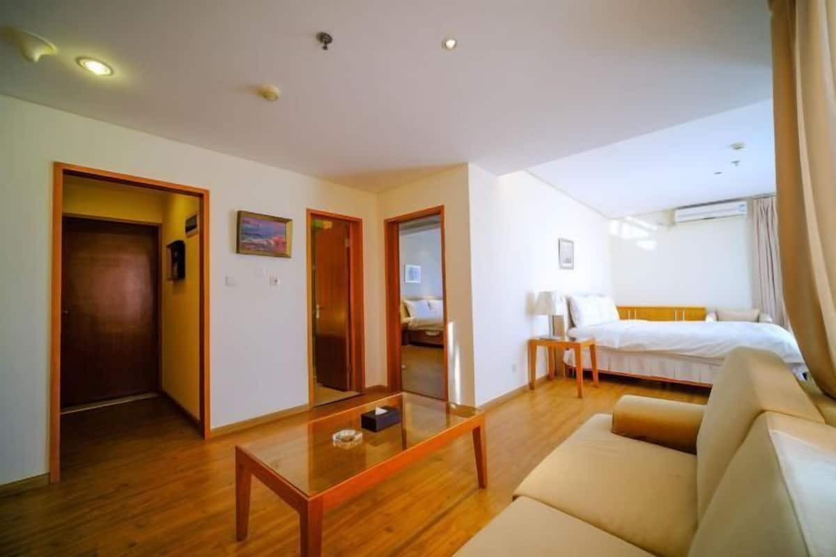 Een hotelkamer met een houten vloer, een bank, een bed, een kleine tafel en een spiegel.
