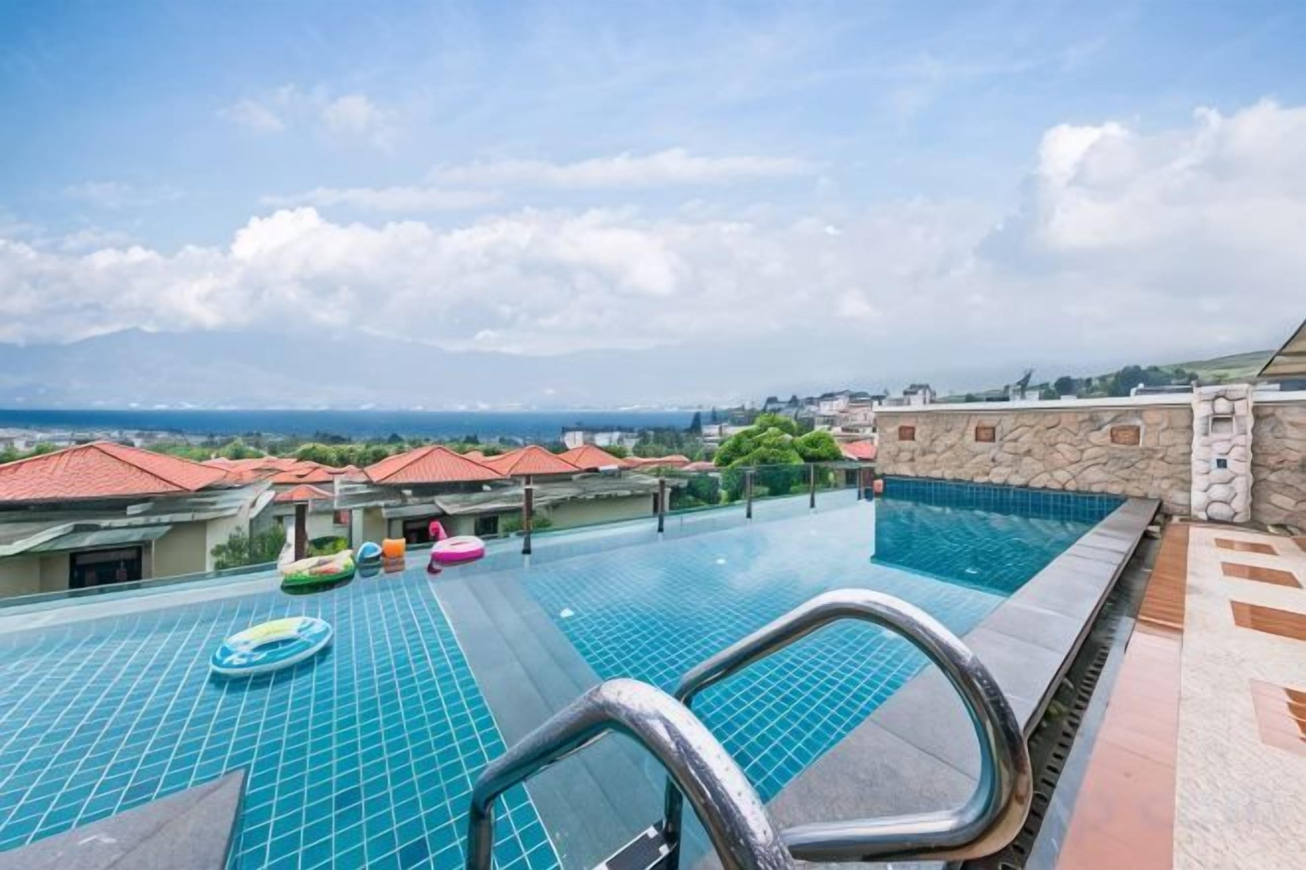An infinity pool with a view of the sea, surrounded by buildings with red roofs.