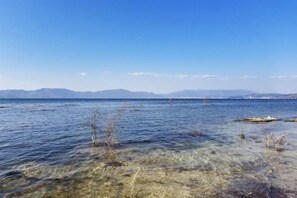 A clear view of a lake with distant mountains, a rocky shoreline, and sparse vegetation. - Huzhiyun Hotel (Chengjiang)
