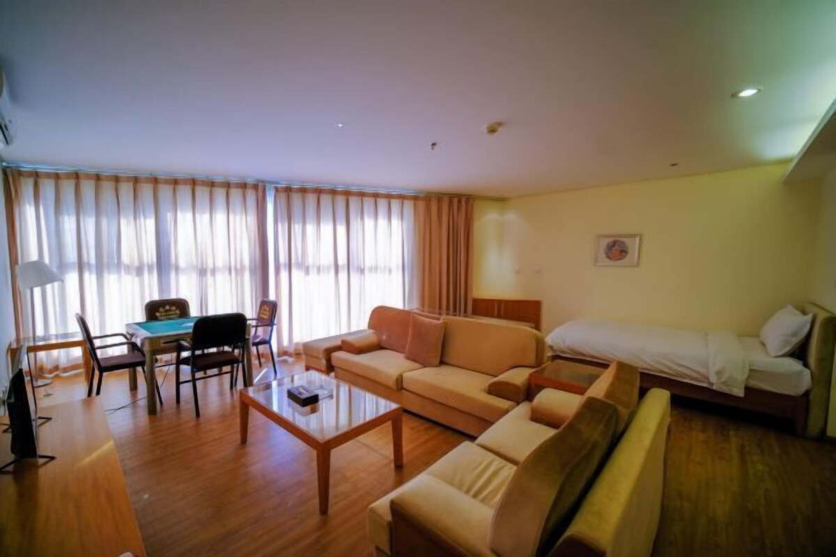 A hotel room with a sofa, a small table, a bed, a desk with chairs, and a window with curtains.