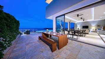 Un espacio exterior moderno con comedor, piscina y vistas al océano.